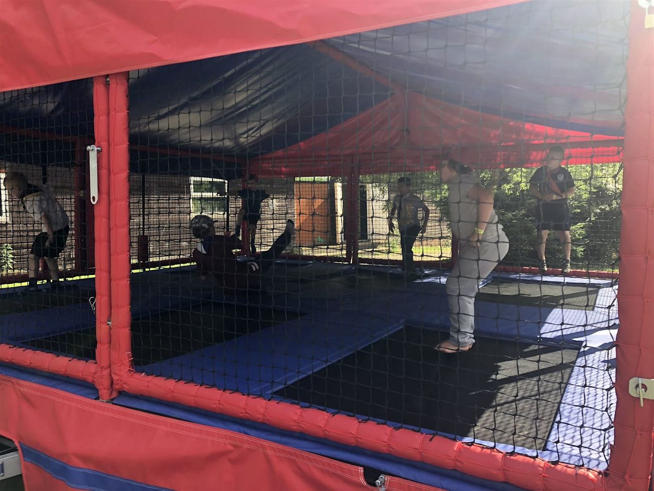 Six children mid-bounce in the trampoline bays, seen through the black safety netting with a brick hall behind