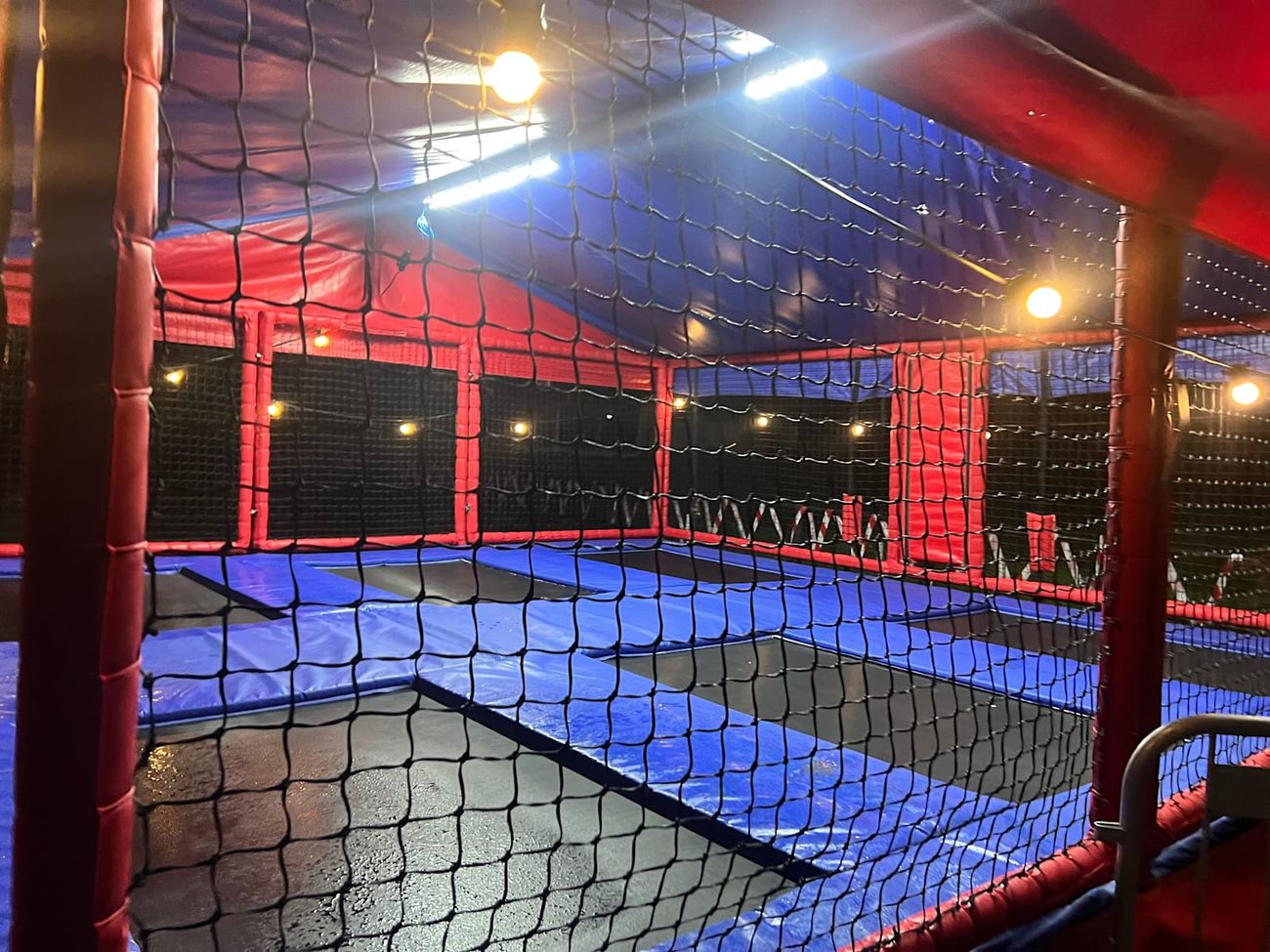 The empty trampoline bays lit by warm string bulbs and white LED strips during an evening session, seen through the netting