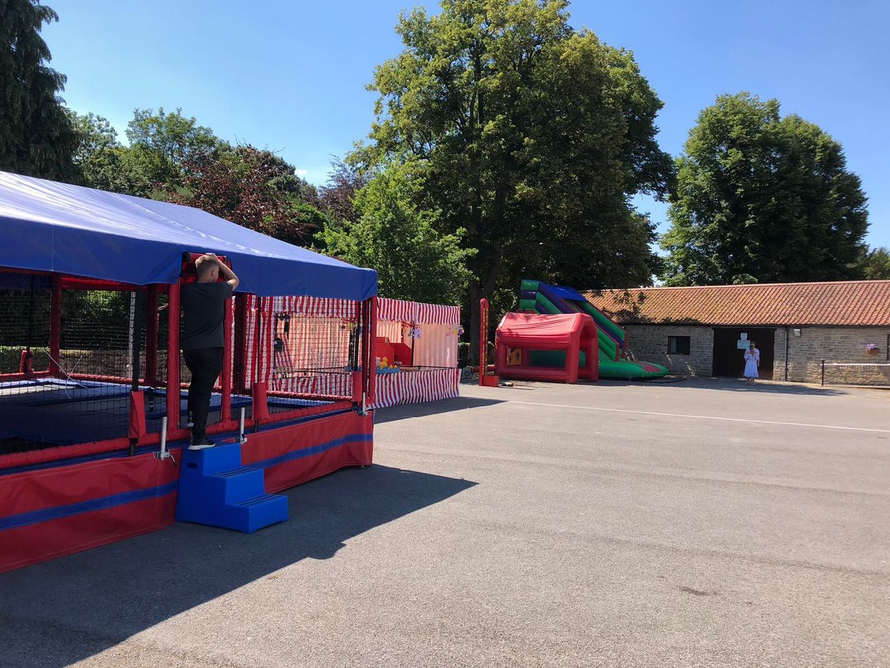 The trampoline set pitched at a village fete on tarmac, beside a candy-stripe side stall and an inflatable slide