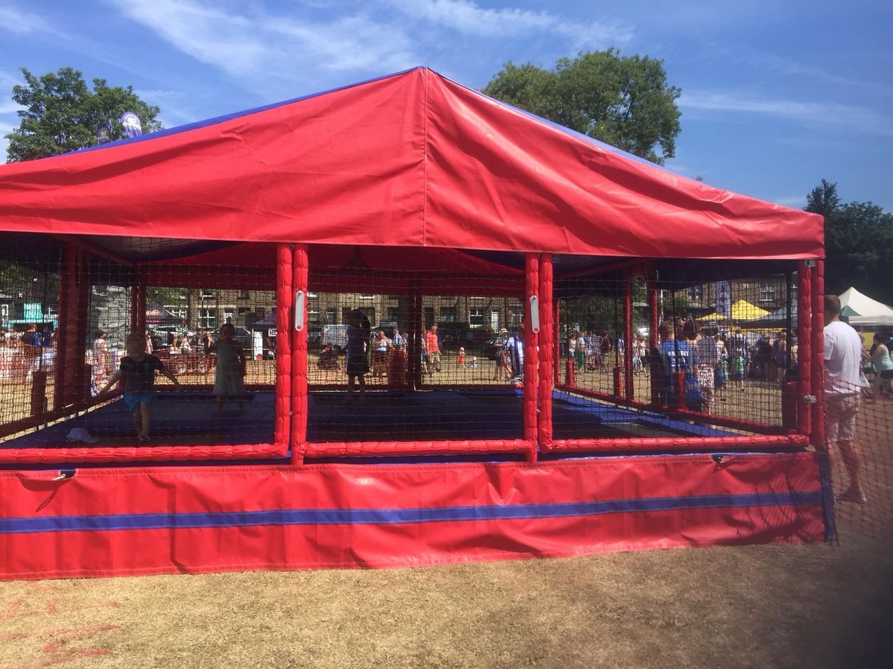The trampoline set trading in bright sun at a country fair, with children bouncing and the stalls and tents beyond