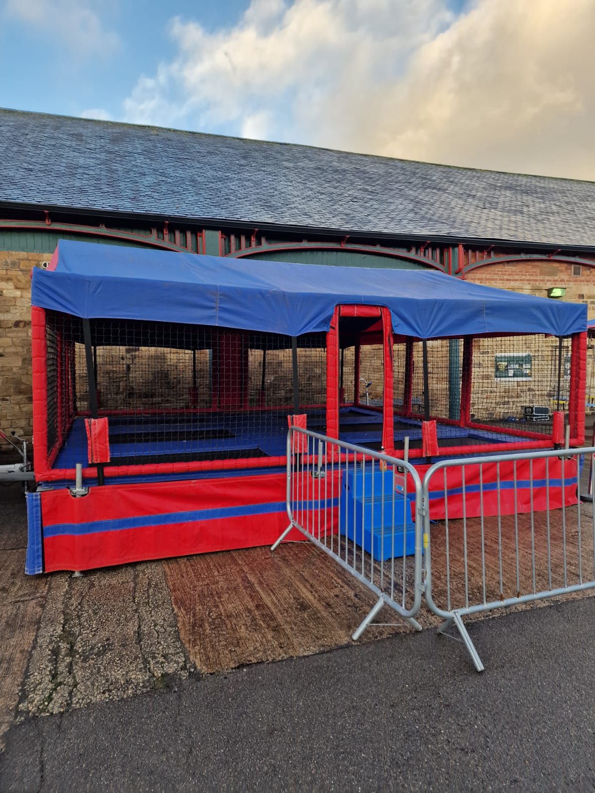 The trampoline set in a heritage station yard at sunset, with the low golden sun catching the red and blue canopy