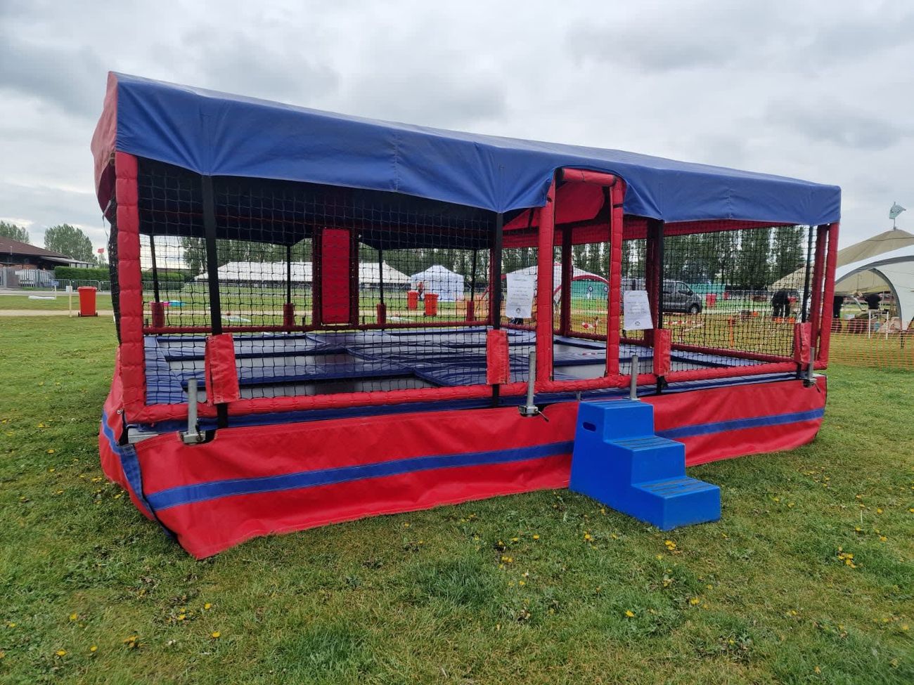 The trampoline set on an overcast showground field, with the event marquees and safety fencing across the grass behind