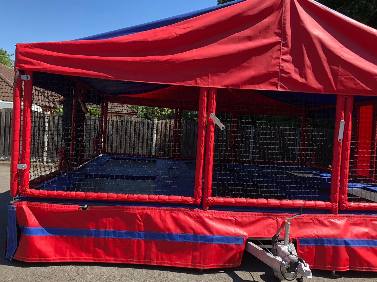 The trampoline set on its trailer on a paved drive, with the tow hitch and jockey wheel visible at the front