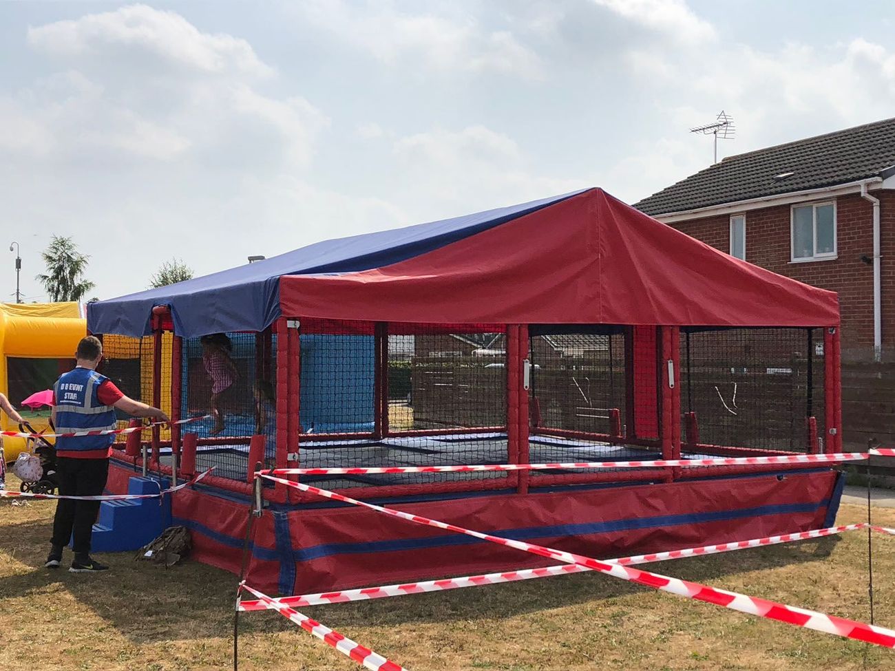 The trampoline set roped off with red and white tape at a family funday, with a steward in a hi-vis vest at the entrance