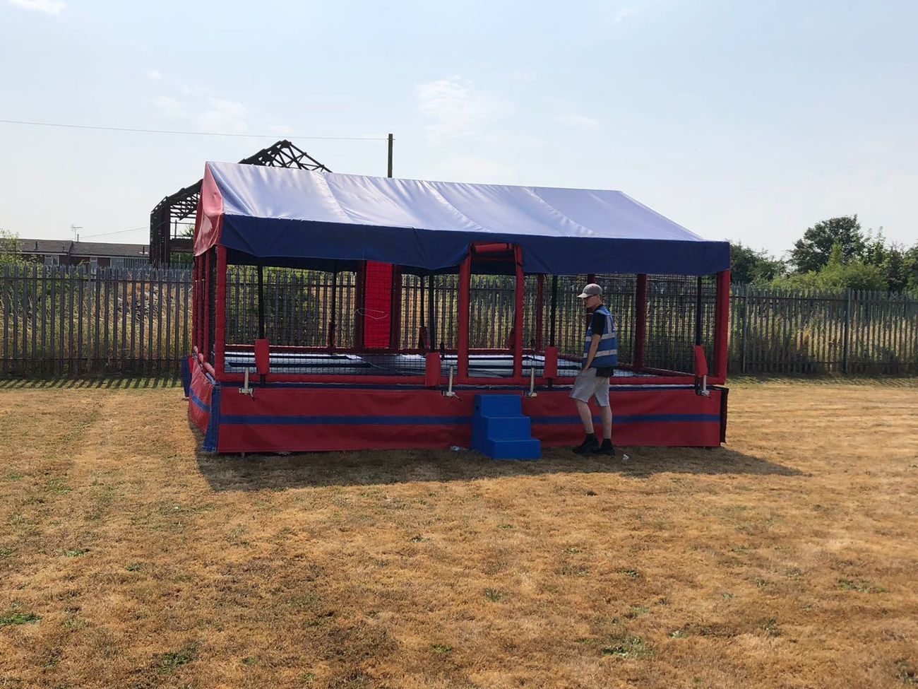The six bed trampoline set on a dry grass field, with its red and blue canopy over the netted bays and the blue entrance steps
