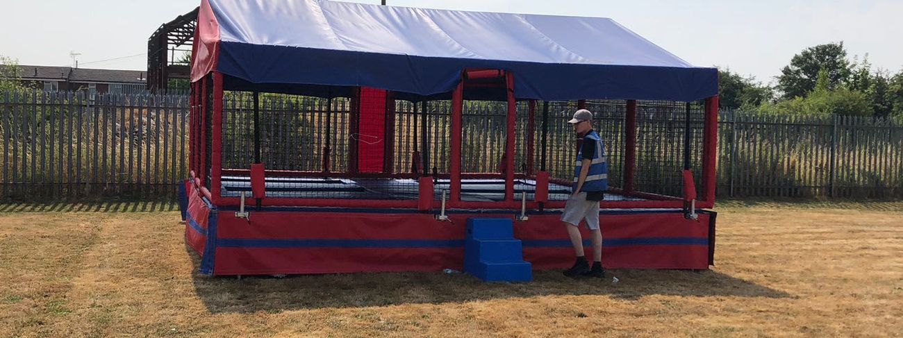 The six bed trampoline set on a dry grass field, with its red and blue canopy, netted bays and blue entrance steps