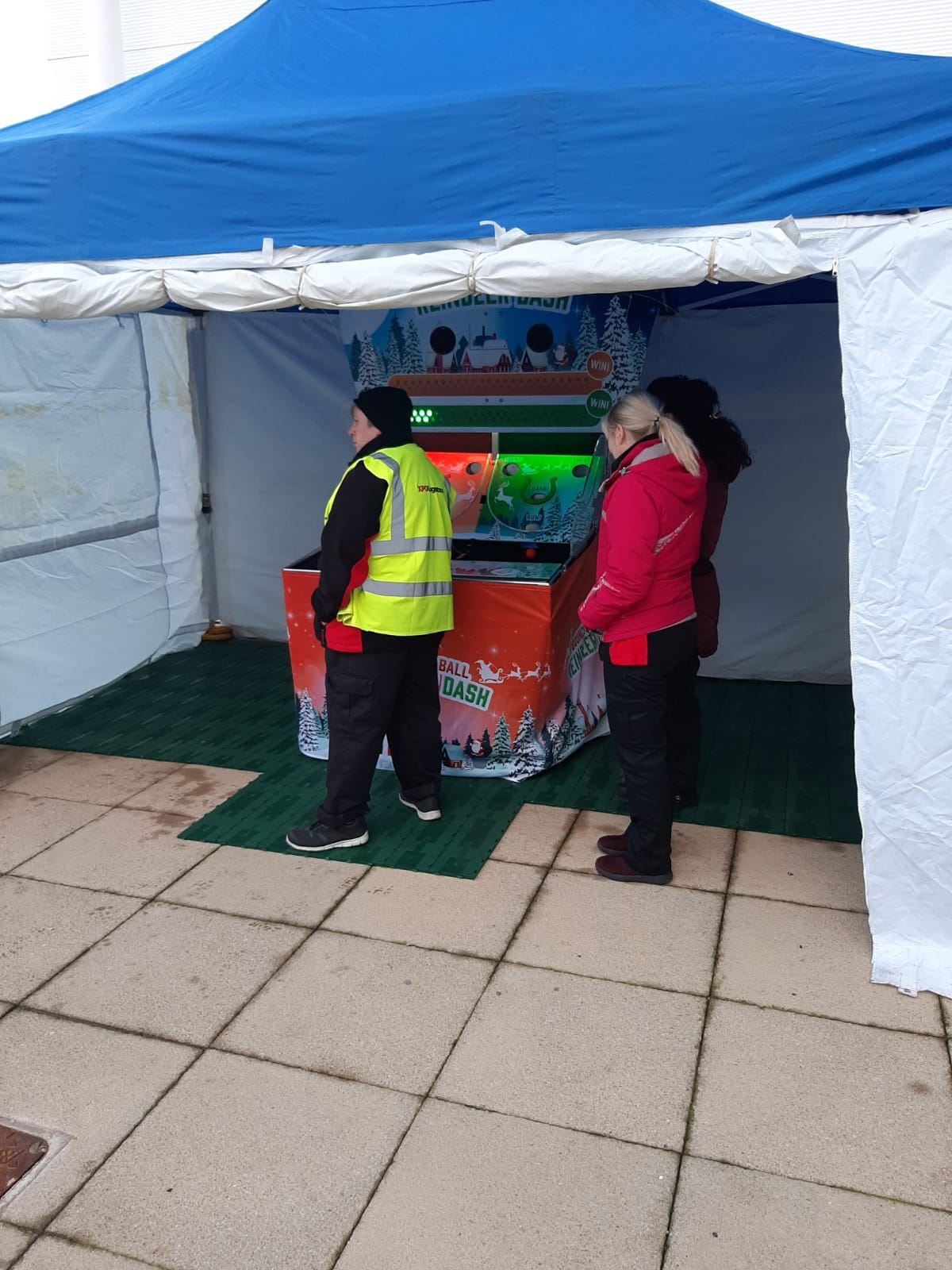 The Bounce A Ball Reindeer Racing cabinet set up outdoors under a gazebo, with an attendant supervising play