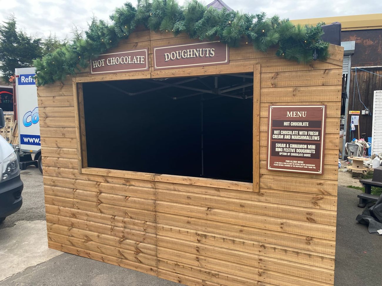 Christmas market stall dressed as a hot drinks and doughnuts hut with a lit garland over the serving hatch
