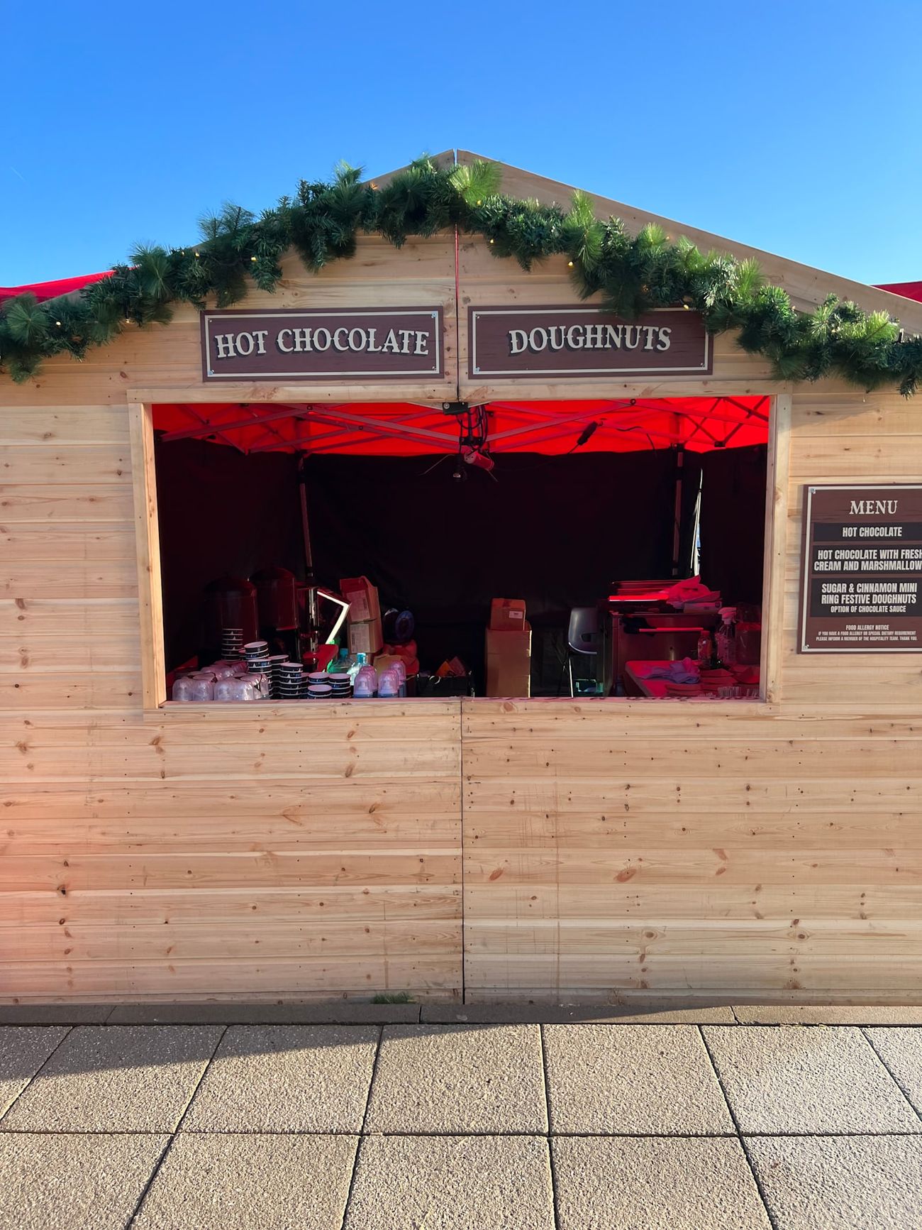 Stocked Christmas market stall on a bright day with the red-lit interior showing through the hatch