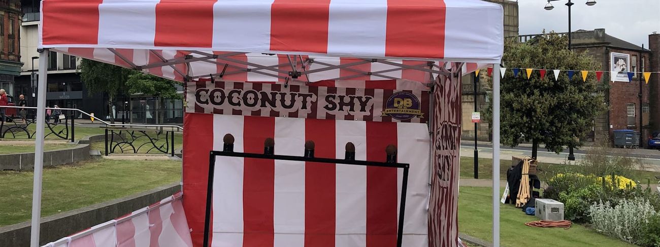 Coconut shy stall set up on grass at an outdoor event with players in shot