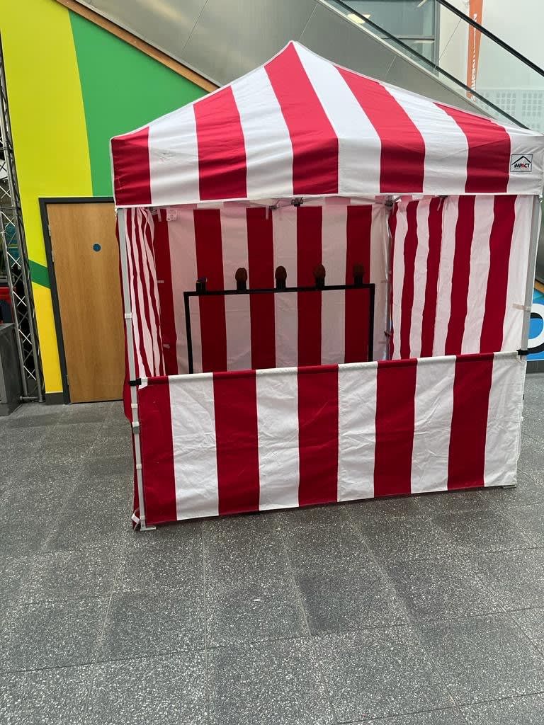 Coconut shy stall under its red and white striped canopy, with coconuts balanced on stands behind the striped counter