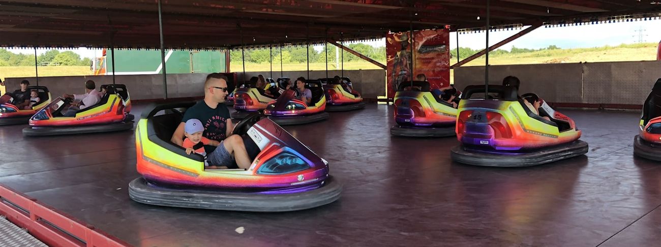 A parent and child riding a dodgem car together on a fenced track