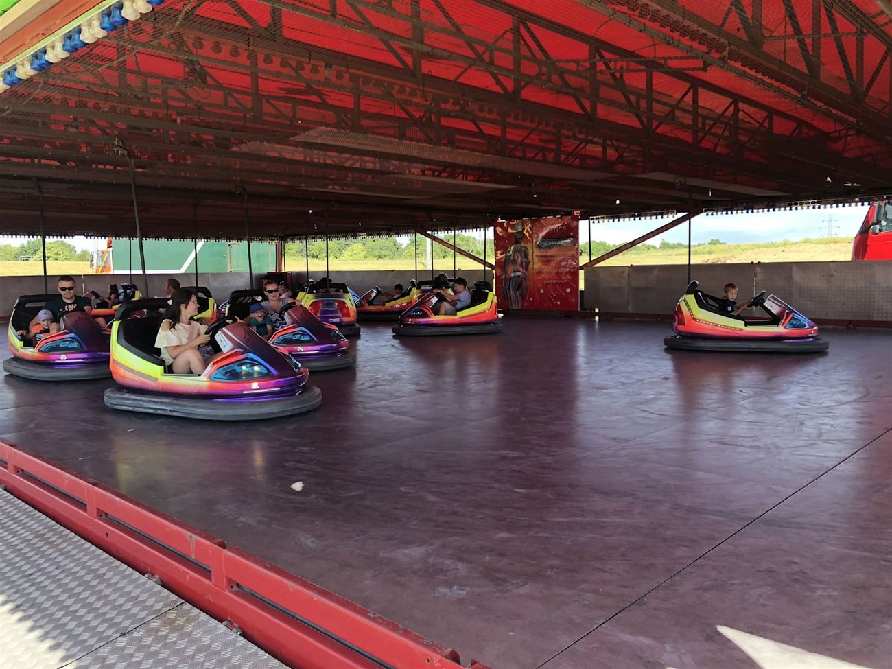 Adults and children driving two-seat dodgem cars beneath the red rink canopy