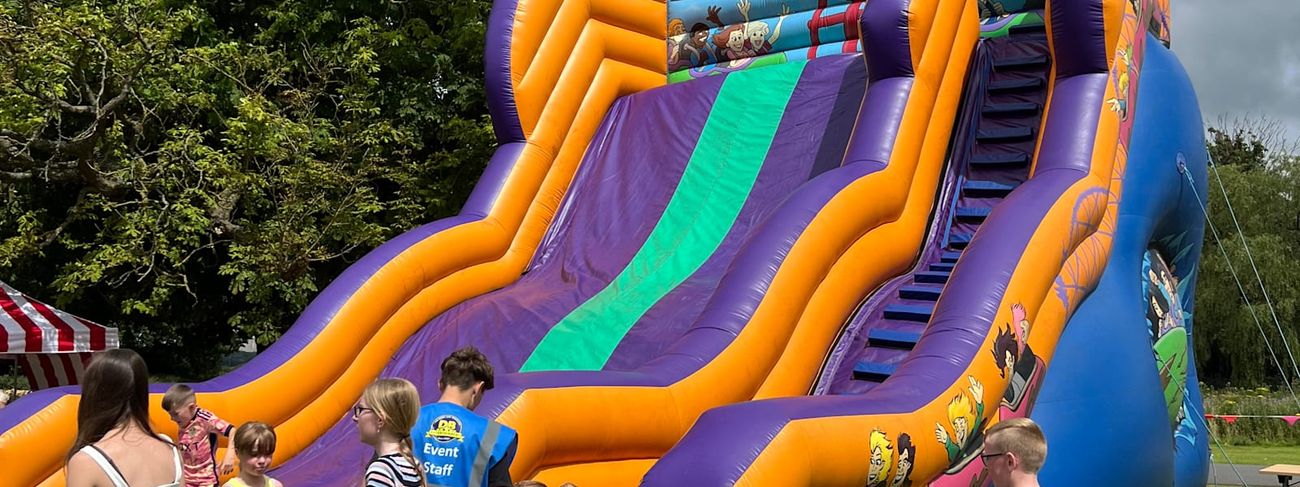 Double-level mega slide set up outdoors, showing the full purple, orange and blue structure with steep stairs, slide lanes and cartoon roller coaster artwork