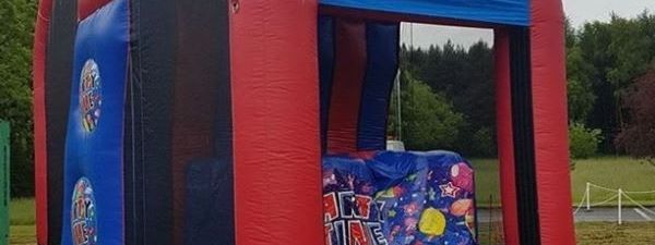 Extreme Base Jump inflatable set up outdoors, showing the red, blue and black structure with its climb, platform and landing pillows
