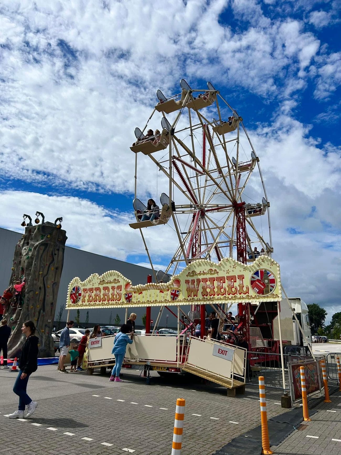Mobile ferris wheel operating on hard standing with riders in open gondolas and separate entry and exit ramps