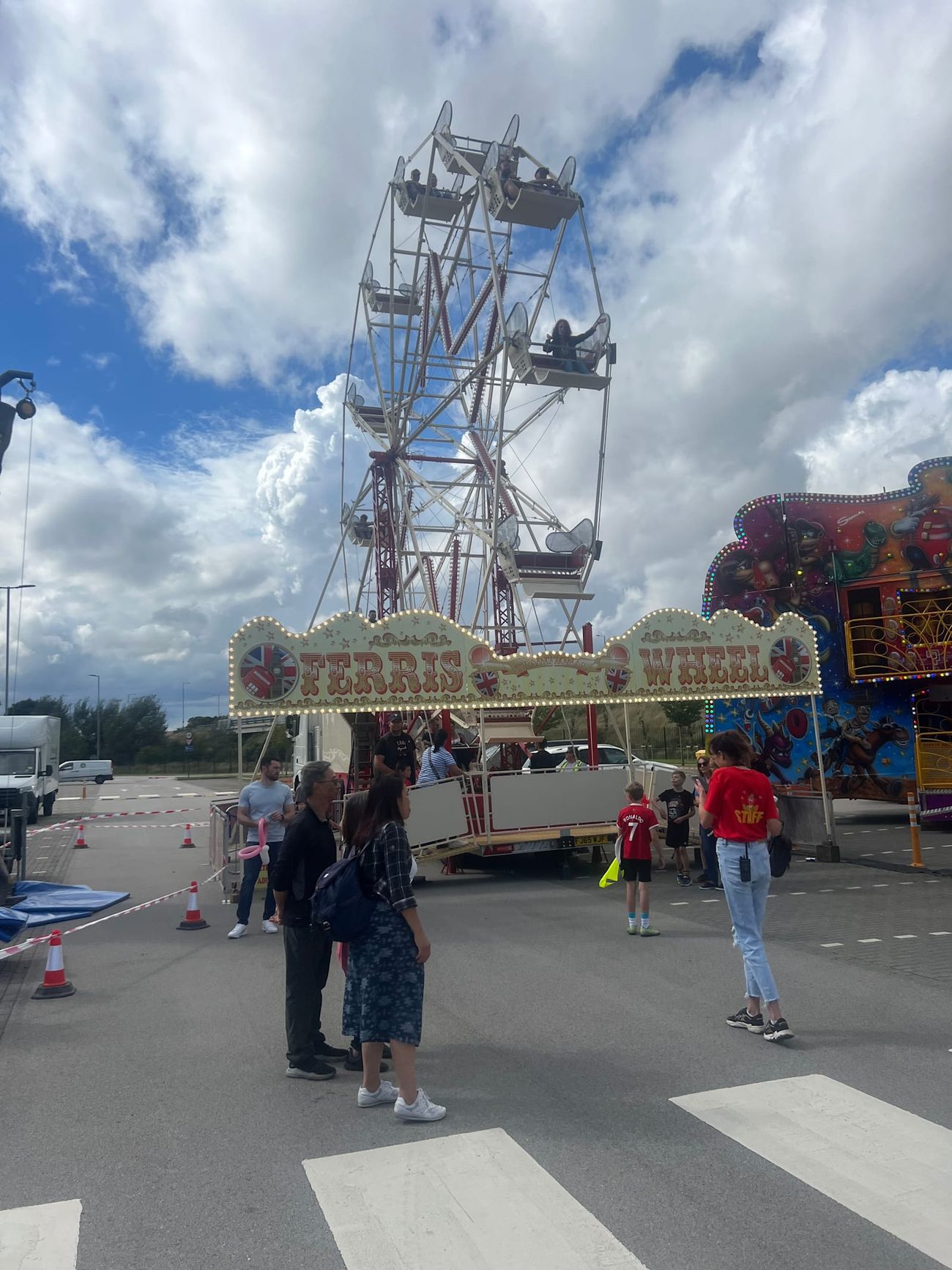 Riders seated in open bench gondolas around the cream ferris wheel frame beneath a cloudy sky
