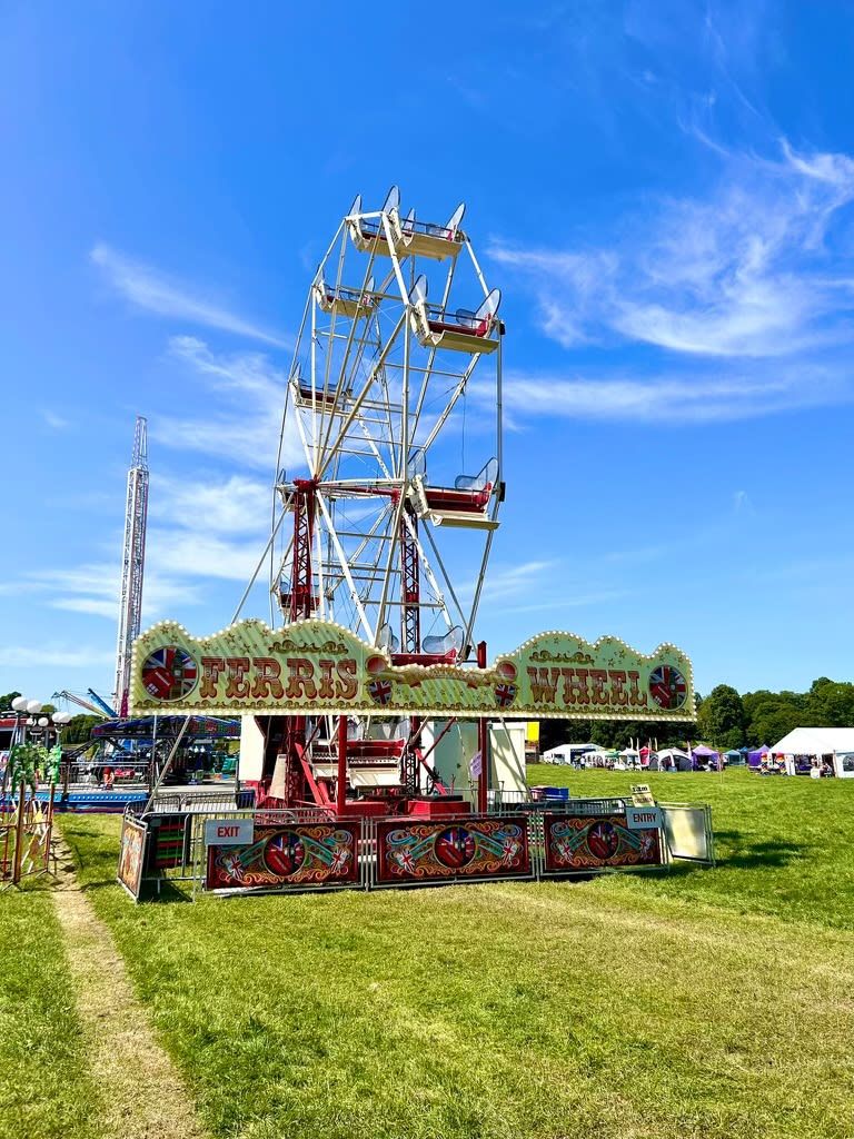 Cream and red mobile ferris wheel set up on a grass showground beneath a clear blue sky