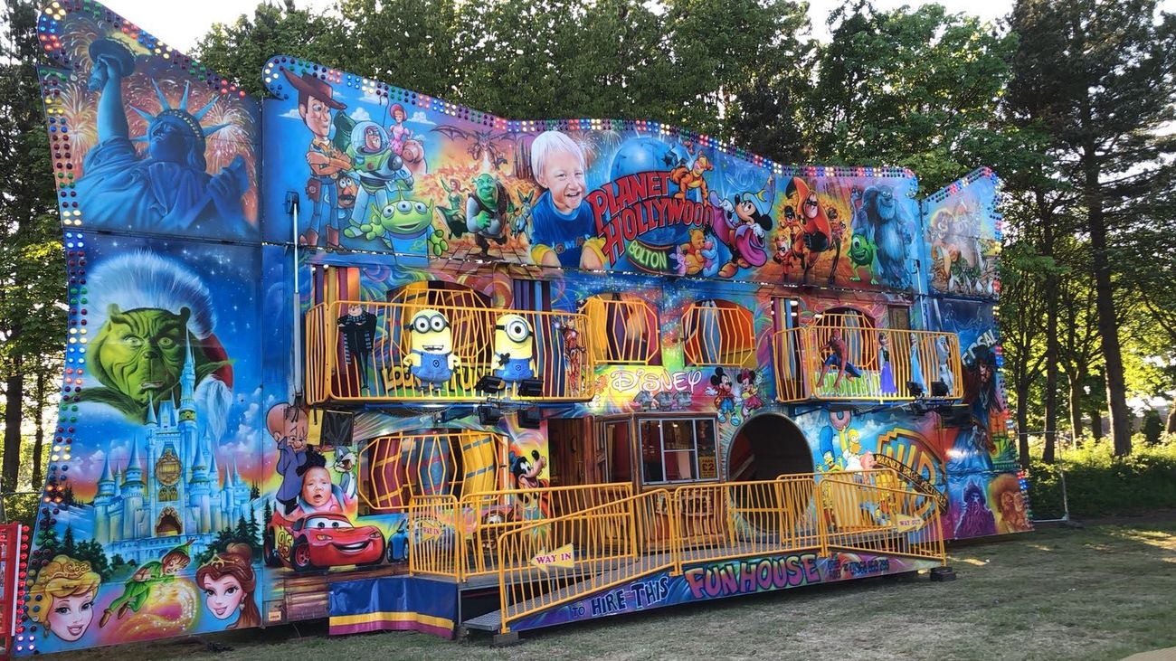 The two-storey funhouse walkthrough on a grass field, with its hand-painted cartoon character frontage, entry kiosk and ramp