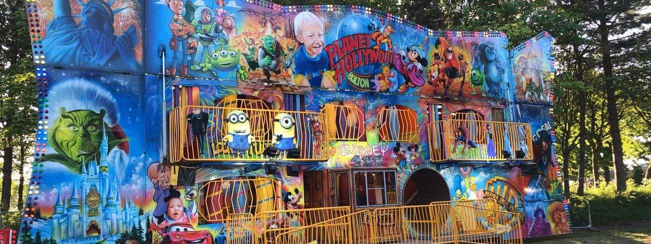 The two-storey funhouse walkthrough on a grass field, with its hand-painted cartoon character frontage, entry kiosk and ramp