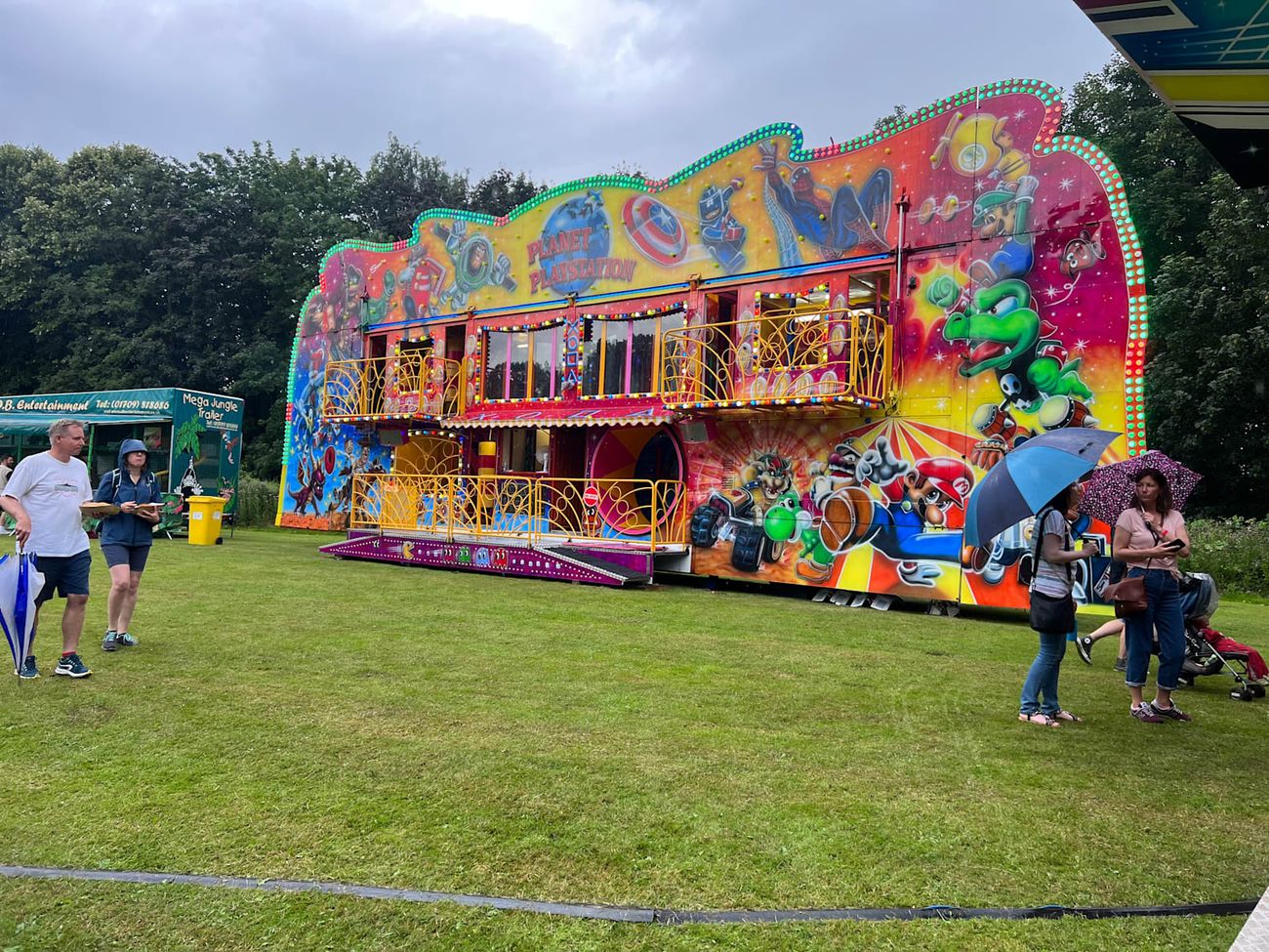 The funhouse frontage standing on wet grass, with its cartoon murals, purple patterned skirt panels and yellow balcony railings