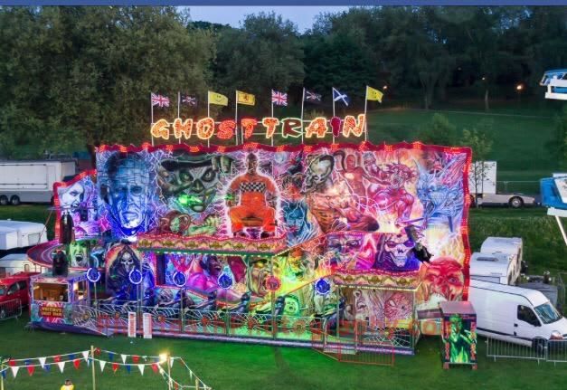 Complete Whiting's Ghost Train illuminated at dusk, with a two-level painted horror frontage, flags and fenced loading platform