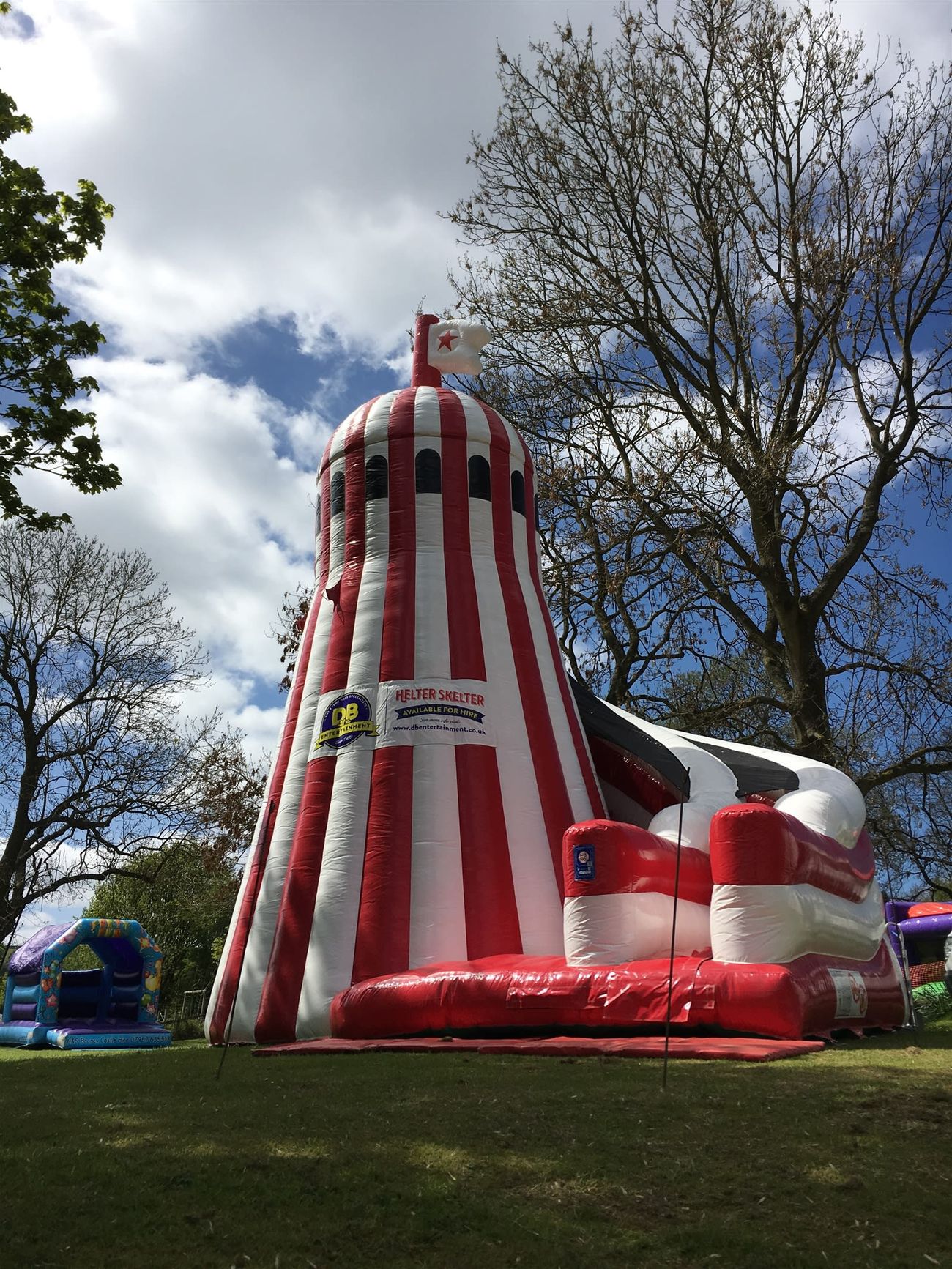 Giant inflatable helter skelter tower on a park event field, with red and white stripes, a spiral slide and a star-tipped finial