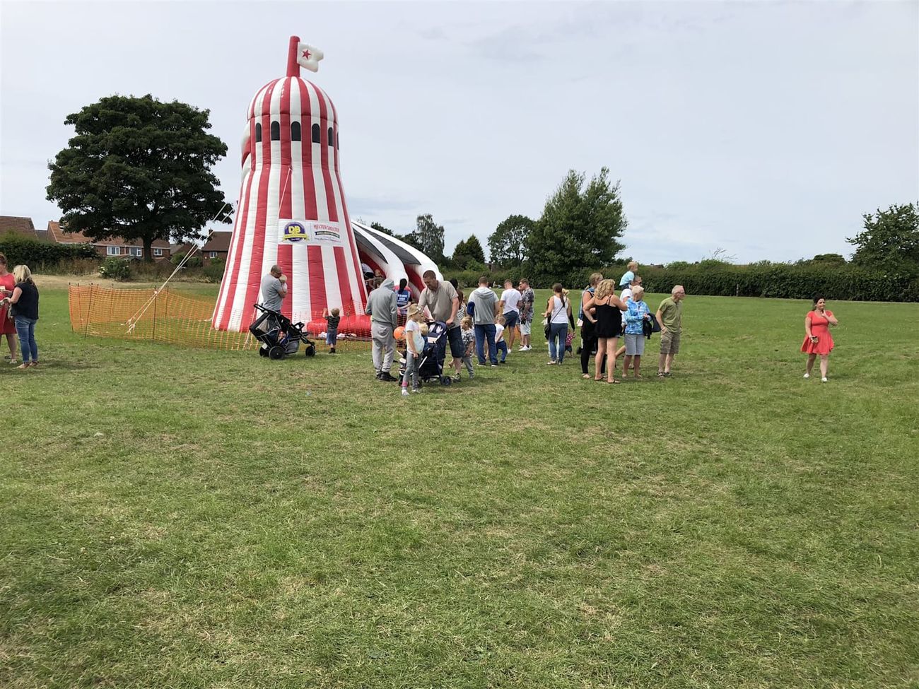 Crowd of adults and children around the helter skelter at a community fete, with its Helter Skelter banner and mesh-fronted slide