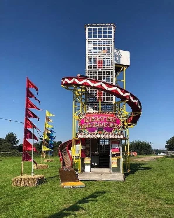 Square-tower helter skelter on grass, with the internal staircase visible through the mesh tower, a red and white spiral slide and a gold Helter Skelter sign