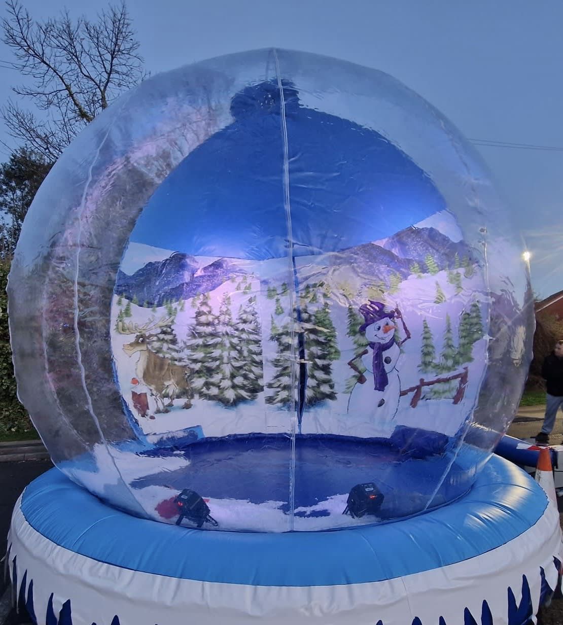 Daytime view through the giant snow globe's clear panels, showing the snowman, wooden fence and mountain backdrop