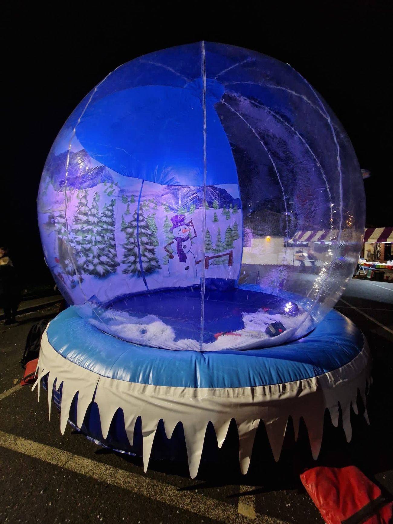 The giant snow globe illuminated at an outdoor evening event, the winter backdrop glowing through the dome