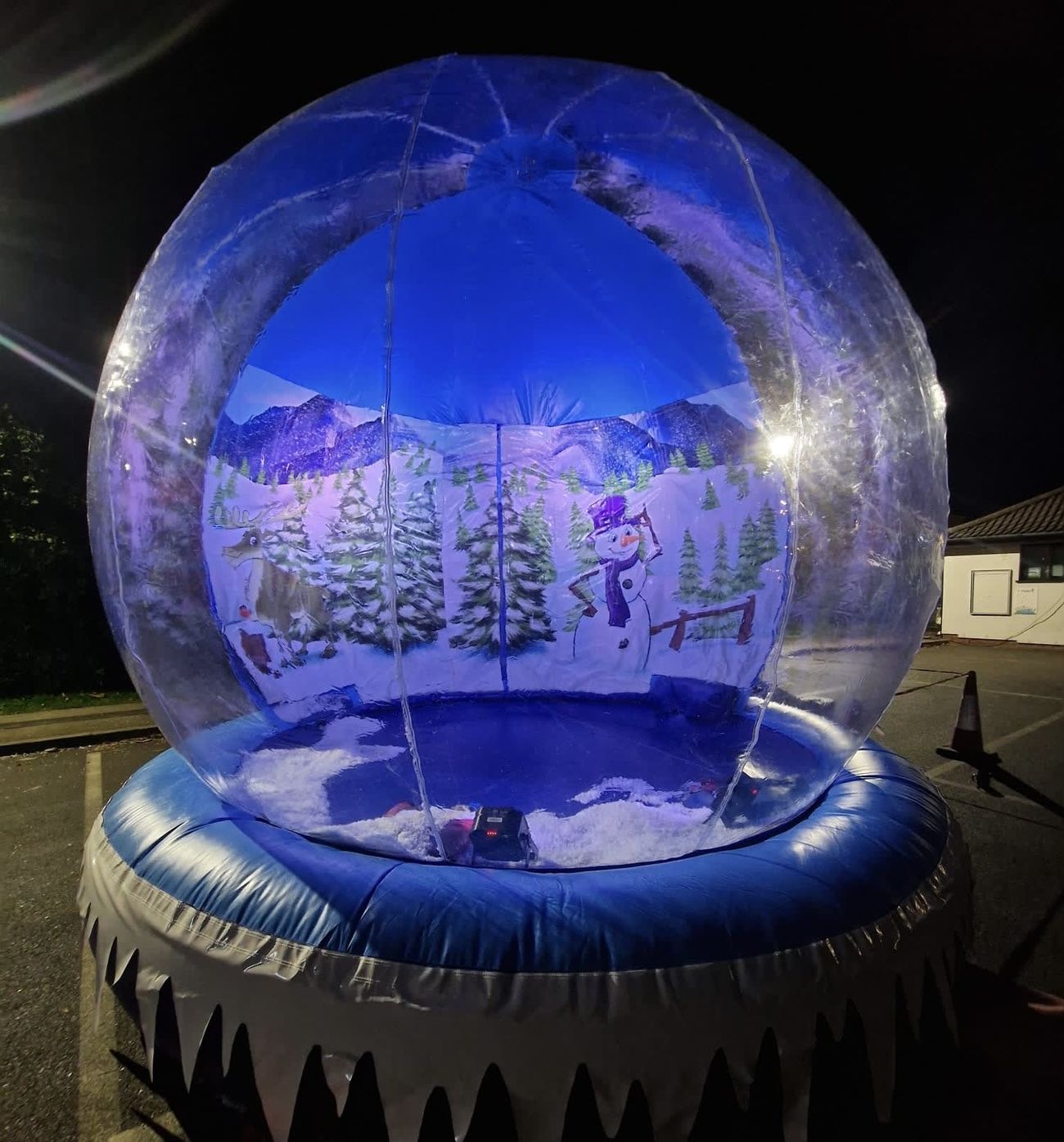 The giant inflatable snow globe outdoors at night with the clear dome glowing blue and the snowman and reindeer visible inside