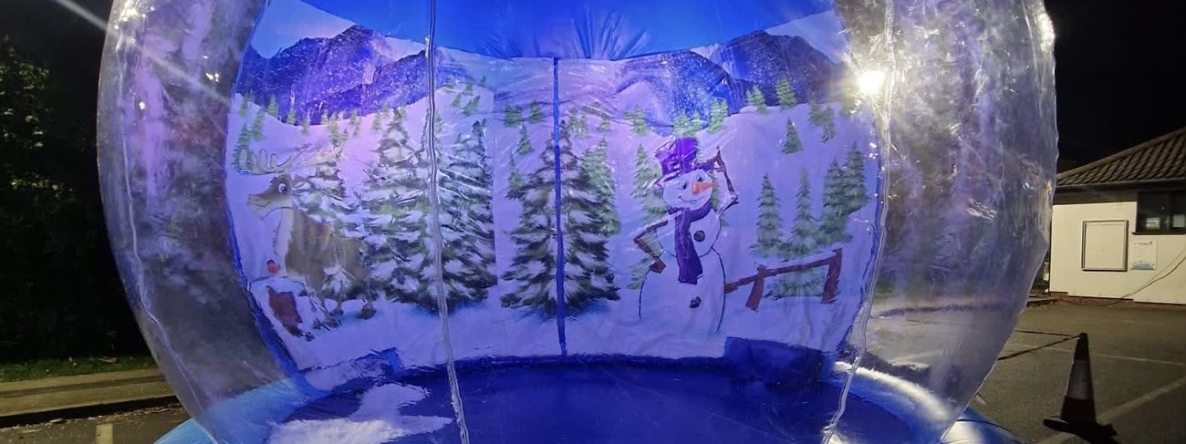The giant inflatable snow globe set up outdoors at night with the clear dome glowing blue, snowman and reindeer visible inside
