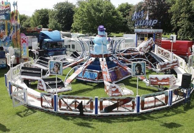 Giant Ski Jump ride on grass with sleigh-style cars on striped arms around a top-hatted snowman centre and snow-covered perimeter fence