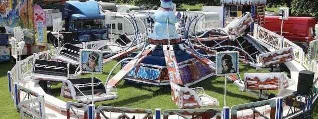 Giant Ski Jump ride on grass with sleigh-style cars on striped arms around a top-hatted snowman centre and a snow-covered perimeter fence
