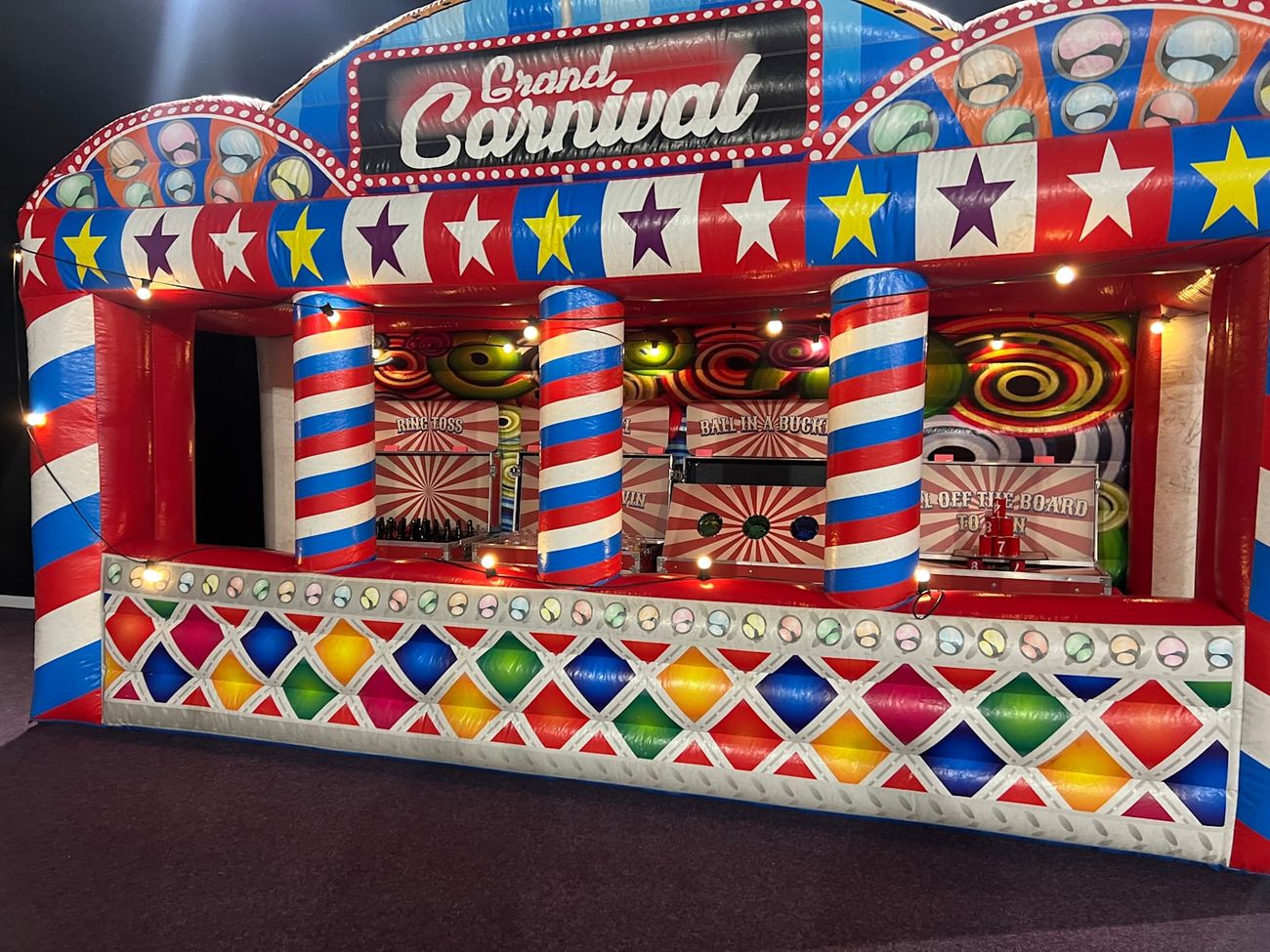 Front of the Grand Carnival stall with its bulb lights lit above the game bays