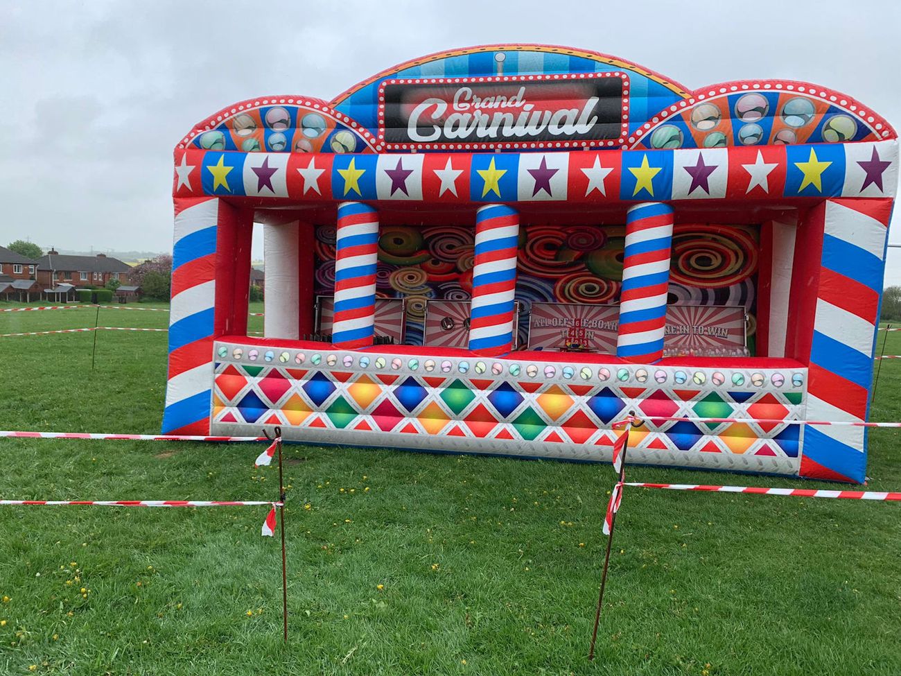 Grand Carnival inflatable stall on an event field, with its marquee-lettered sign, striped pillars and four game bays