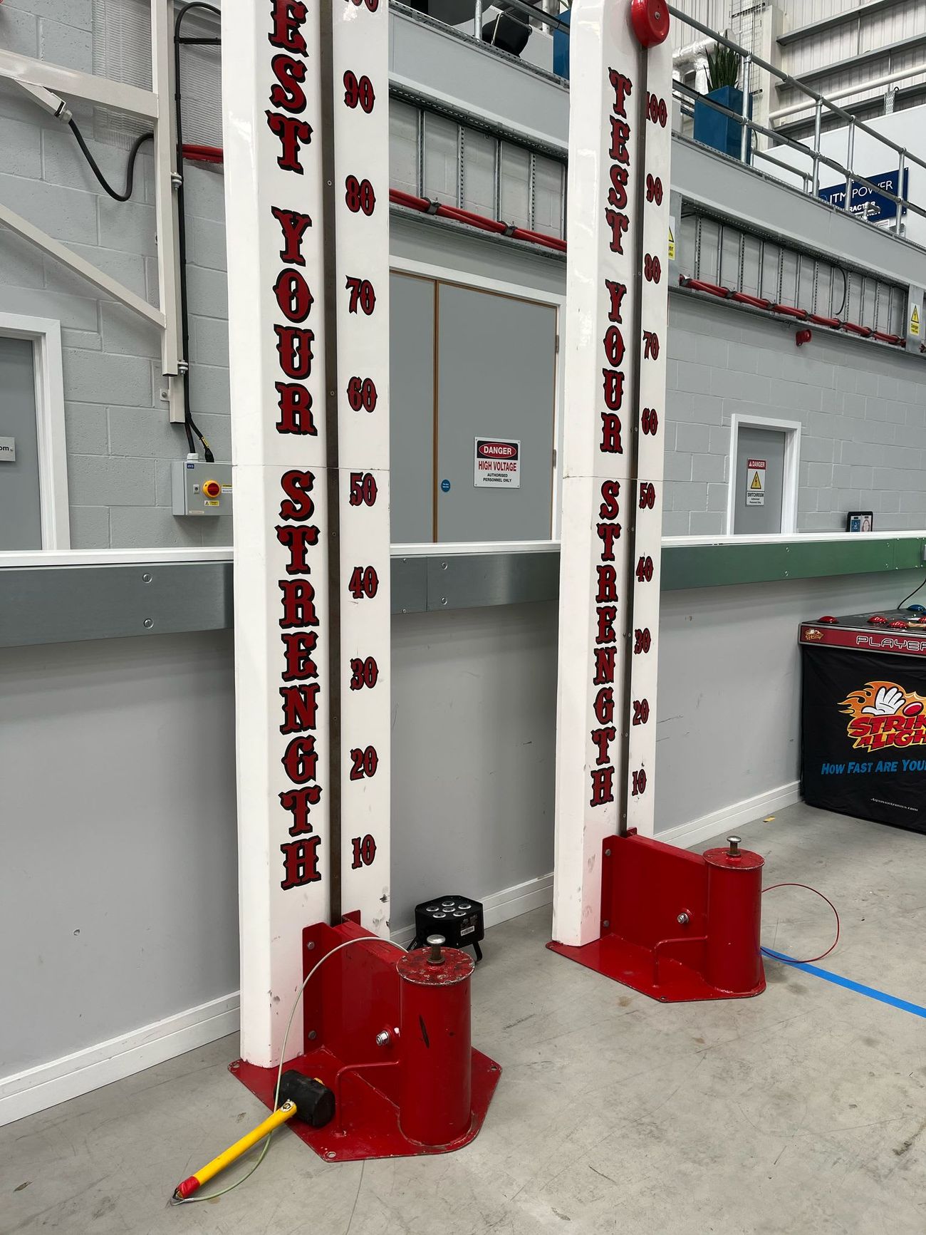 Two High Striker towers standing side by side for a head-to-head, each with its TEST YOUR STRENGTH lettering and bell