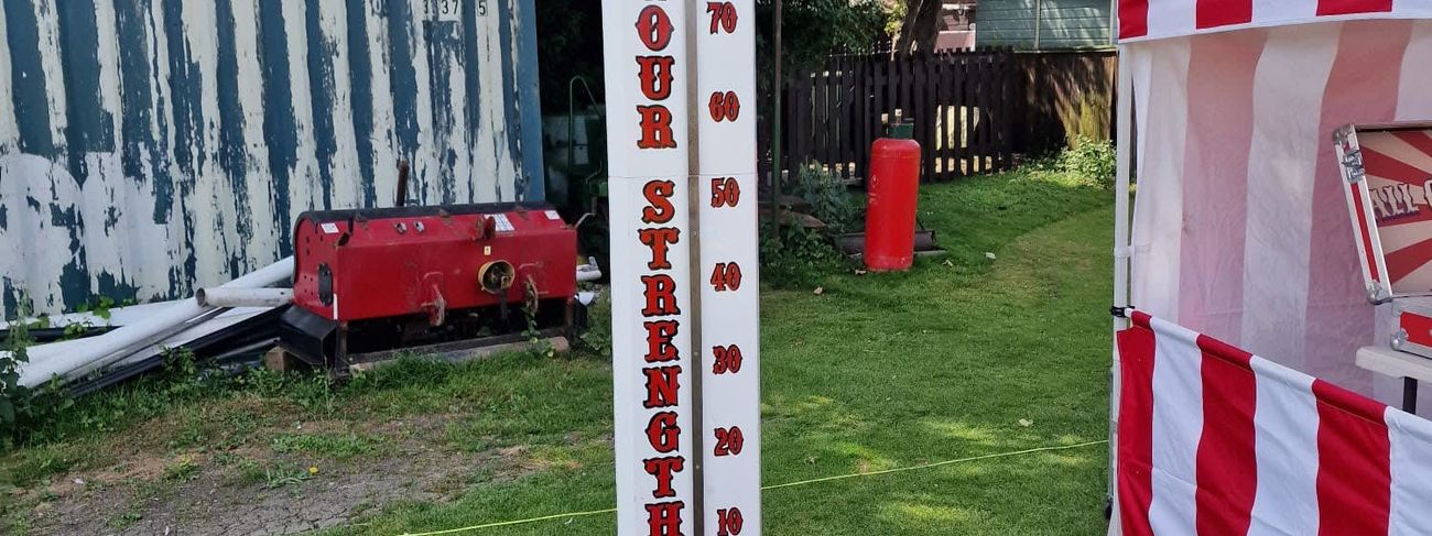 High Striker test-your-strength tower on grass, with its 10-100 scale, mallet on the ground and red bell at the top