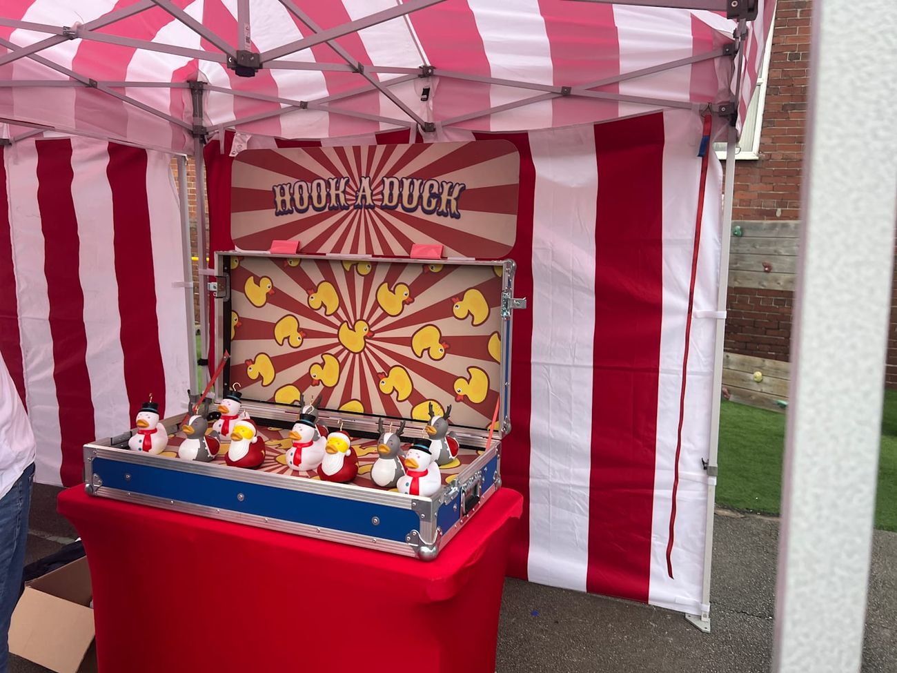 Hook-a-Duck stall under its red and white striped gazebo at an outdoor event, with prizes displayed around the game unit
