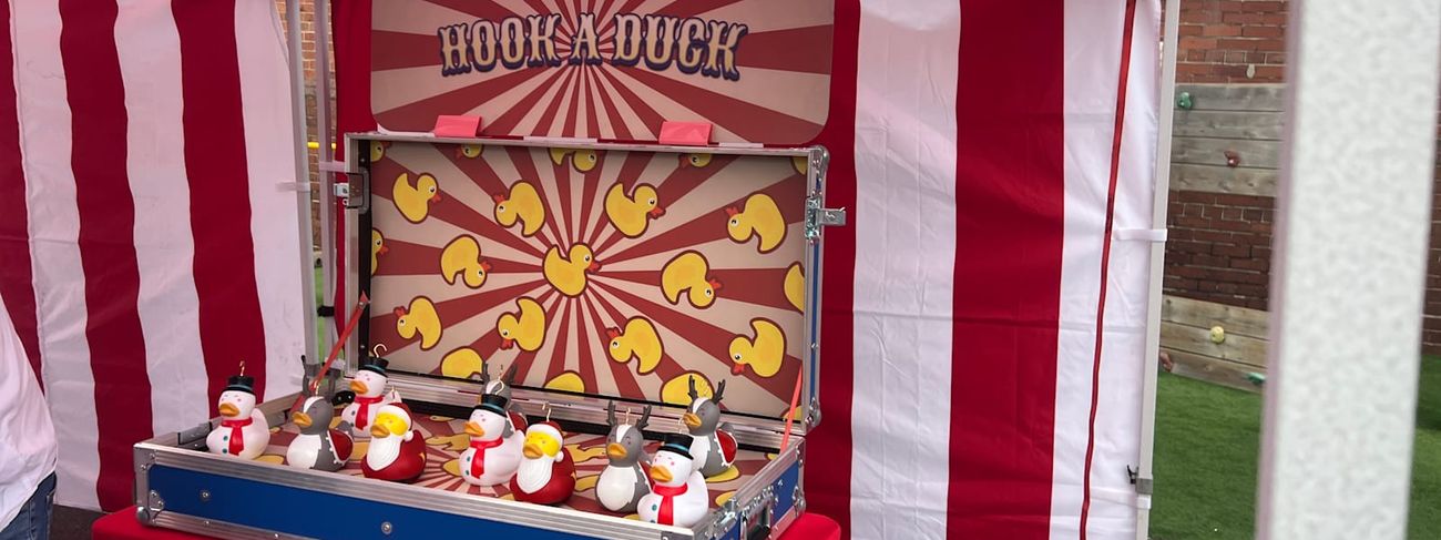 Hook-a-Duck stall under its red and white striped gazebo at an outdoor event, with prizes displayed around the game unit