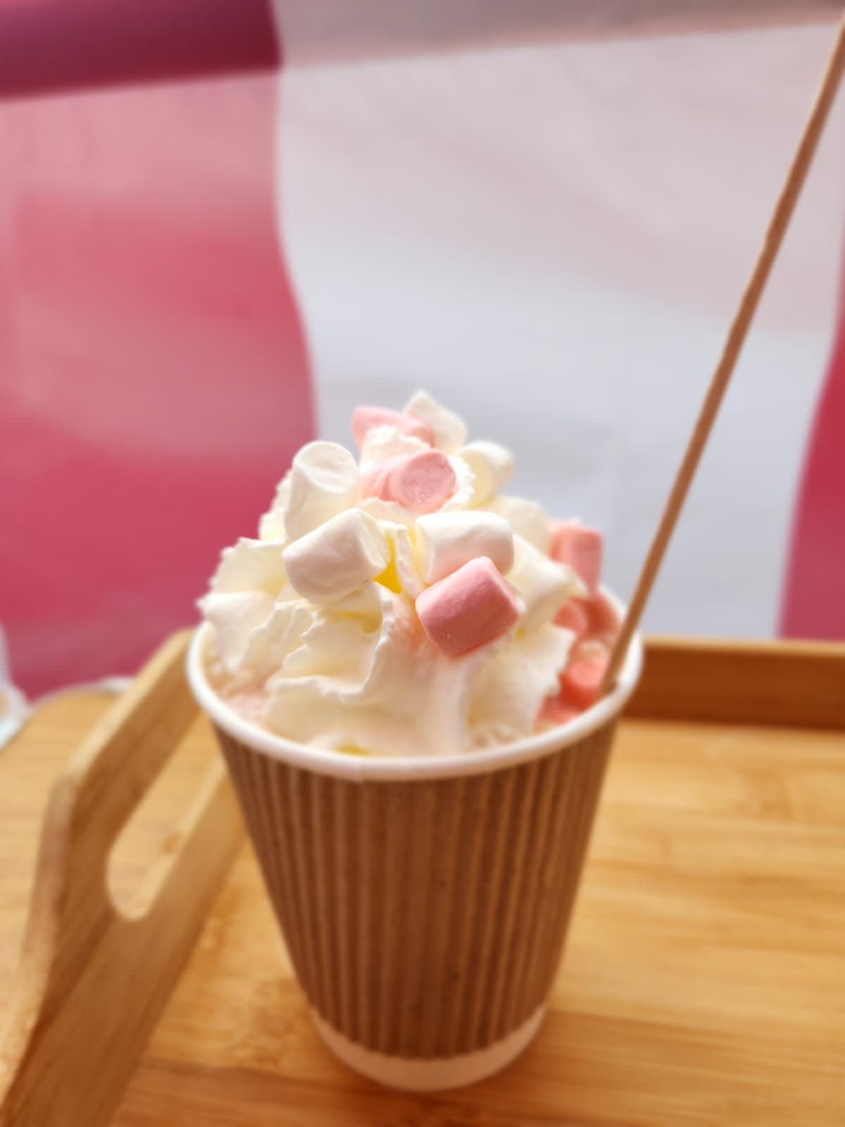 A cup of hot chocolate topped with whipped cream and marshmallows, with a wooden stirrer