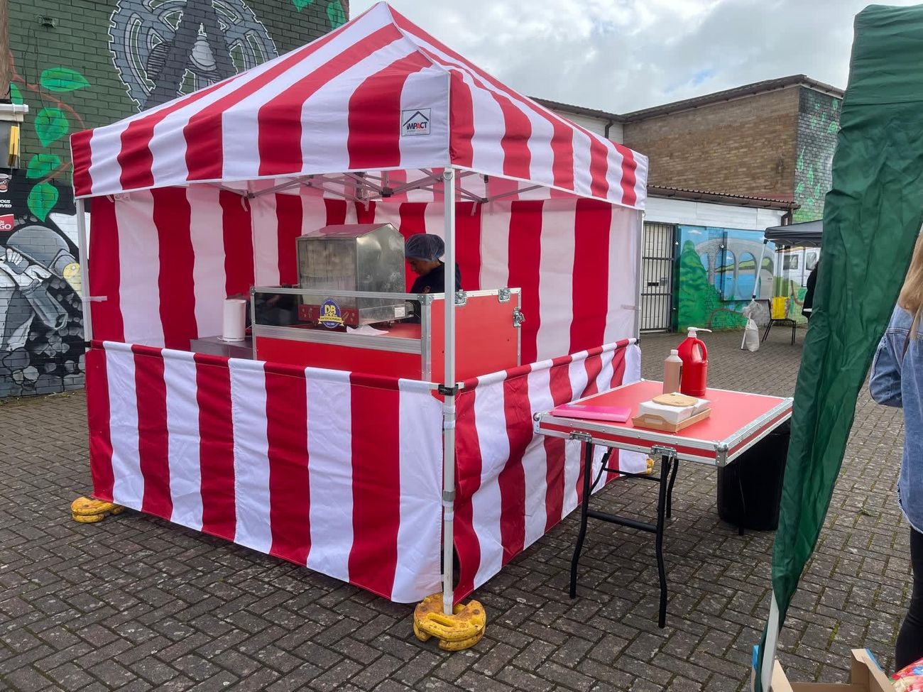 Hot dog stall under its red and white striped gazebo at an outdoor event, with the steamer and serving table set up