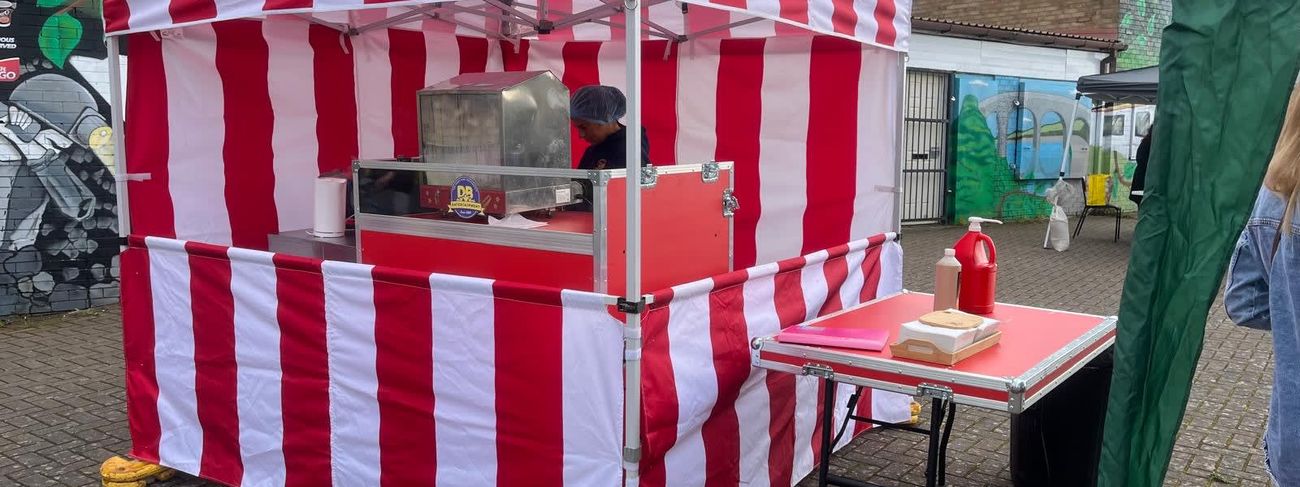 Hot dog stall under its red and white striped gazebo at an outdoor event, with the steamer and serving table set up