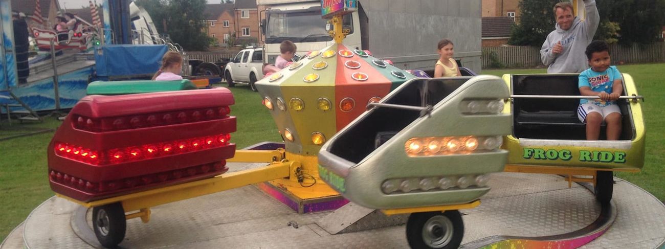 Jump and Smile children's ride with frog-themed cars on a circular platform with a rainbow edge and the Jump and Smile sign on the centre hub