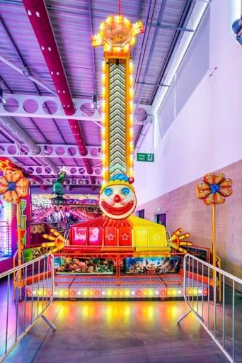 The Jumpin Jack children's drop tower with its clown-face frontboard, red and white striped bulb-lit column and star panels, set up indoors behind queue barriers
