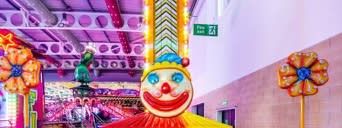 The Jumpin Jack children's drop tower with its clown-face frontboard, red and white striped bulb-lit column and star panels, set up indoors behind queue barriers