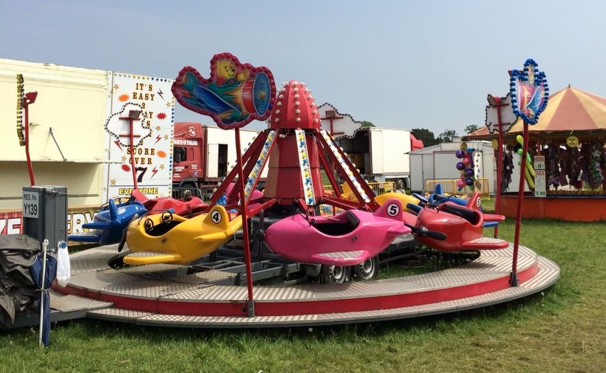 Juvenile flying planes ride on a grass field, with colourful aeroplane carriages on a circular platform with bulb-lit arms