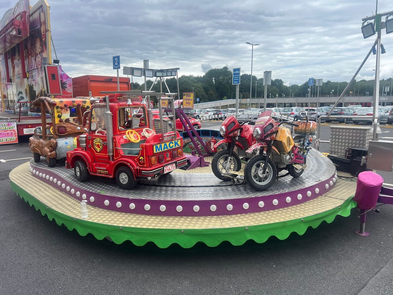 Juvenile Formula children's track ride with fire engine, motorbike and jeep carriages on a circular track with a purple bulb-lit rim