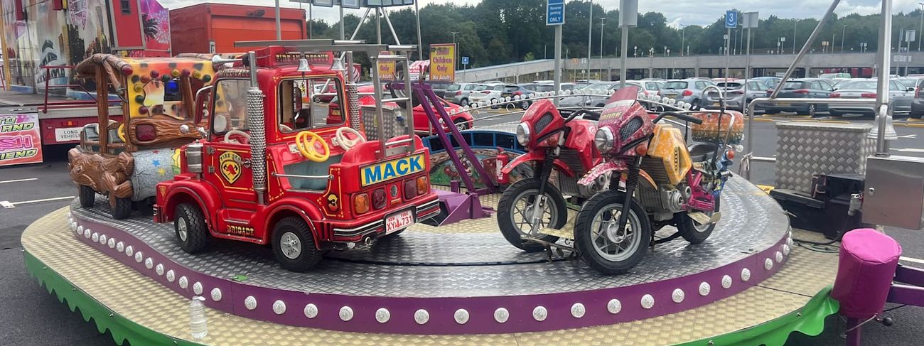 Juvenile Formula children's track ride with fire engine, motorbike and jeep carriages on a circular track with a purple bulb-lit rim